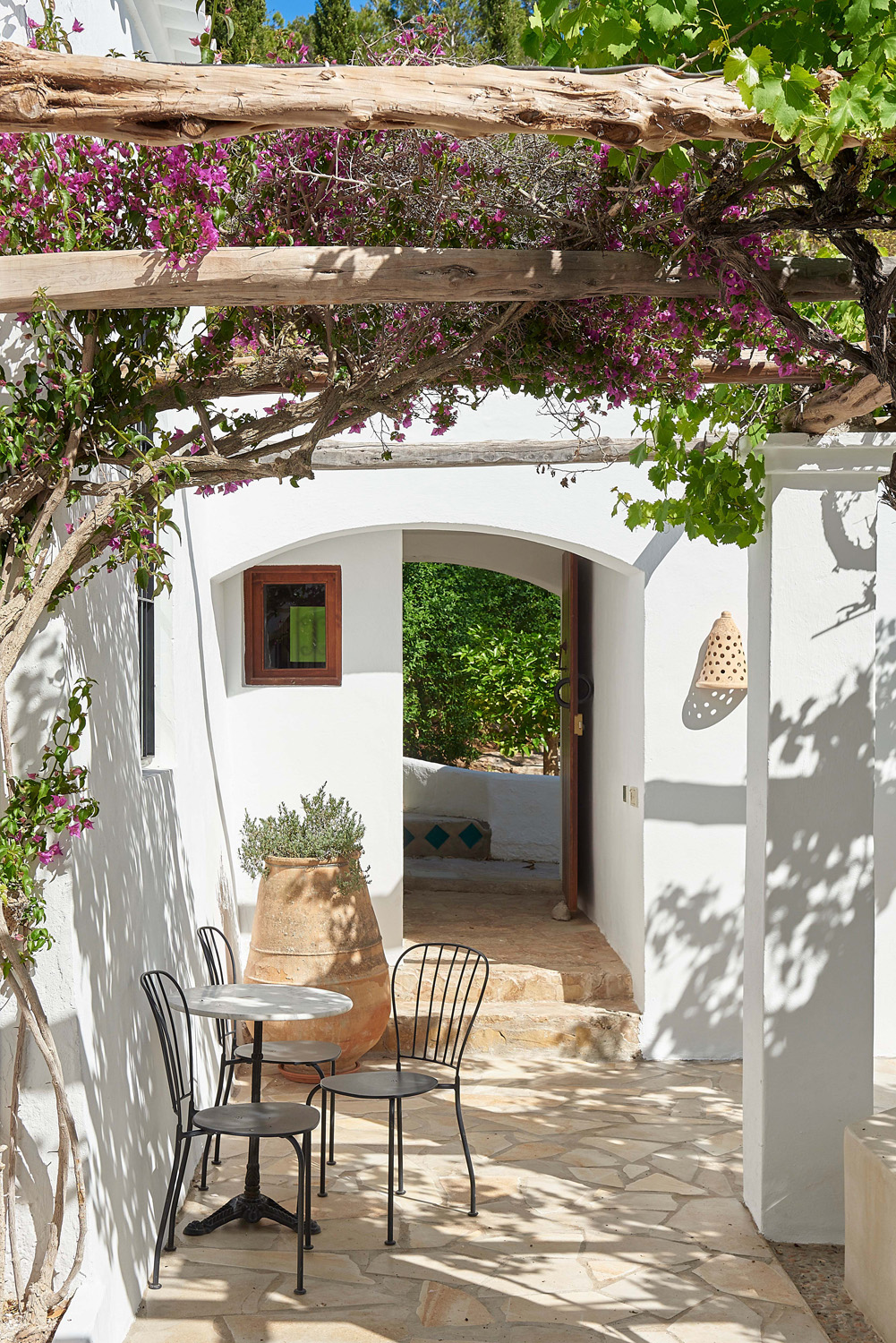 Foliage climbs a pergola above the shaded terrace of an Ibiza villa