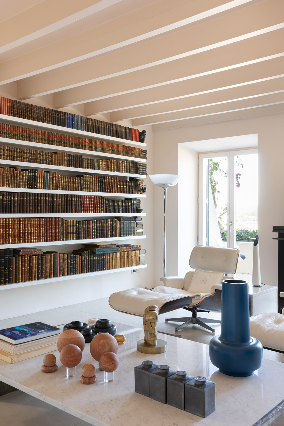 Iconic furniture and curious table sculptures backdropped by a wall of books in a luxury Ibizan townhouse