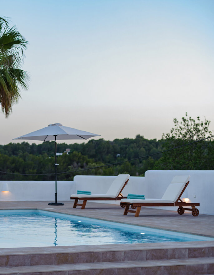 Pool furniture and the greenery of the local area surrounding a luxury holiday home in Ibiza