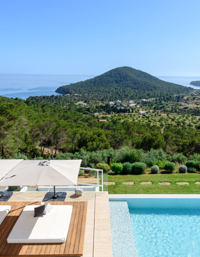 Pool furniture lounges in the sun, backdropped by greenery, at a luxury holiday home on Ibiza
