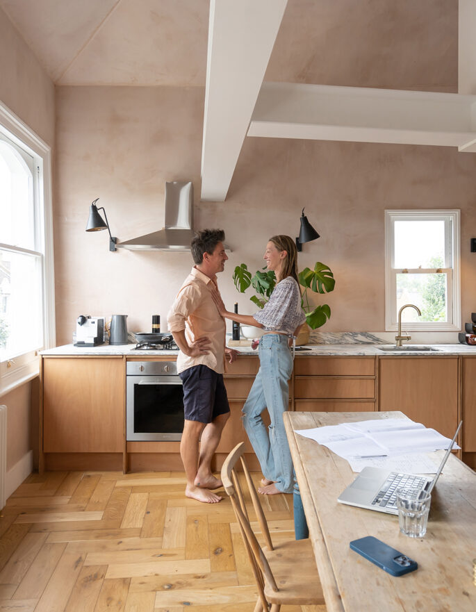 A man and a woman stand in the pastel-pink kitchen of a luxury west London house