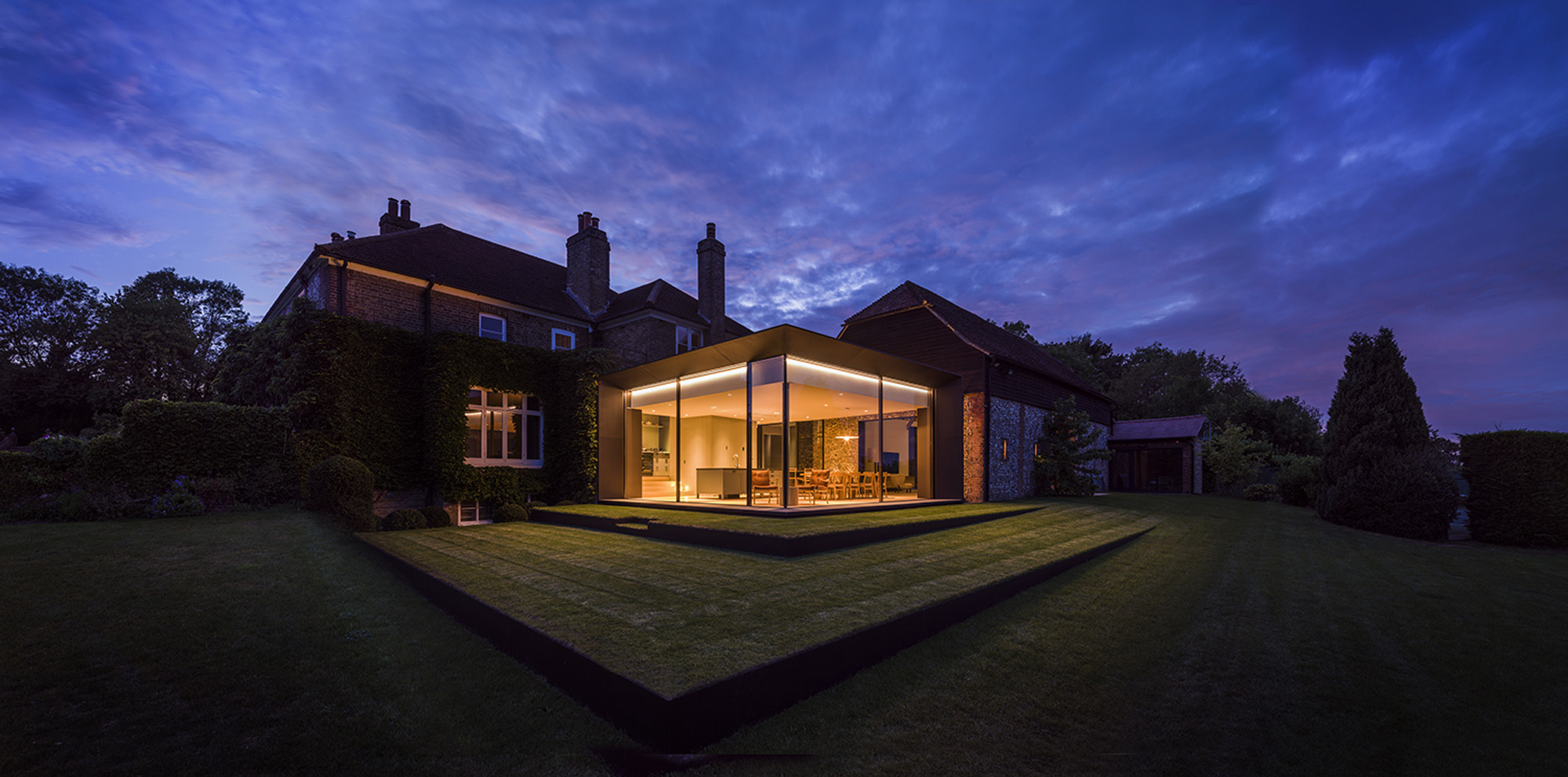 A modern extension to a classic home glows with electric light