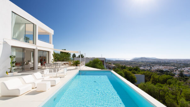 Framed by green, panoramic views, a pool sits next to a luxury villa for sale in Ibiza