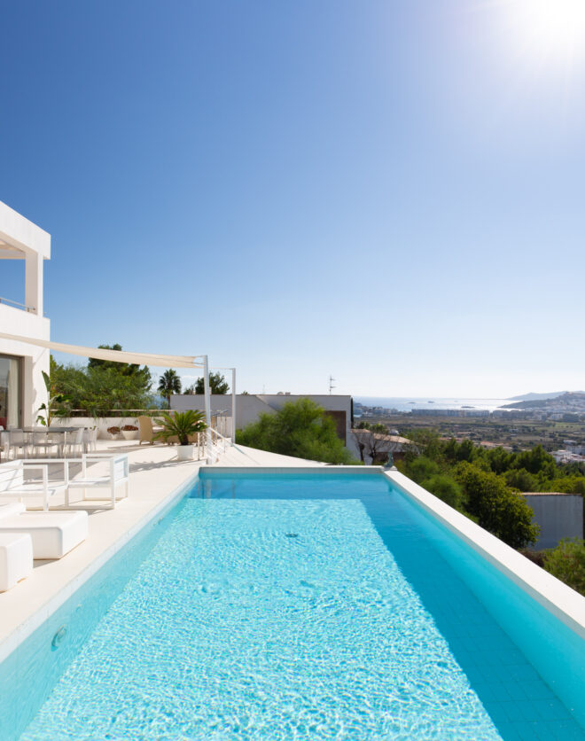 Framed by green, panoramic views, a pool sits next to a luxury villa for sale in Ibiza